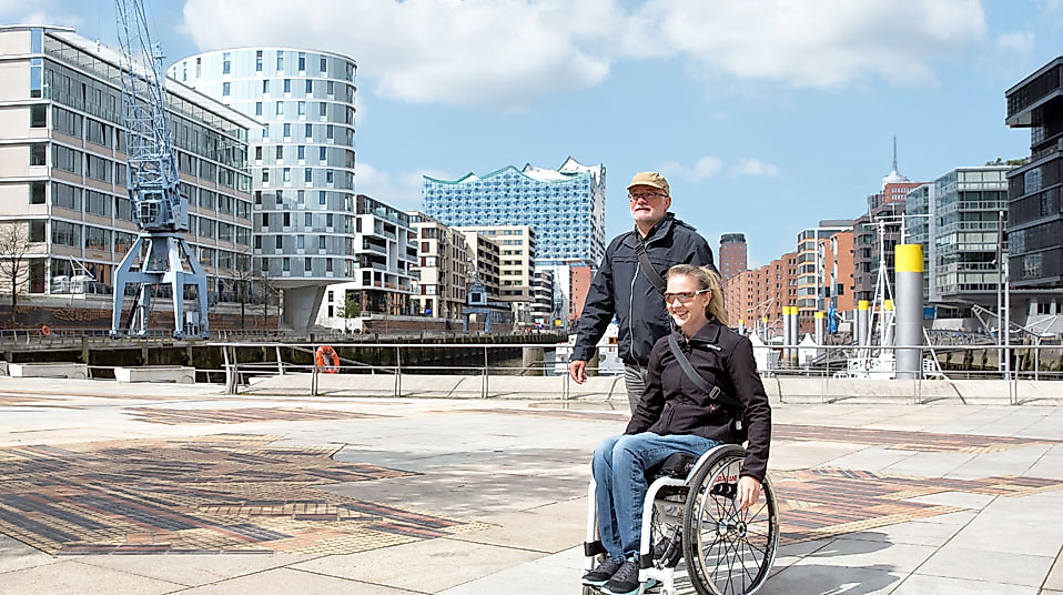 Rollstuhlfahrerin mit Begleitperson auf barrierefreier Tour durch die moderne Hamburger HafenCity.