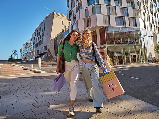 Zwei Frauen schlendern bei Sonnenschein an der Hamburger Alster mit Blick auf Rathaus und Alsterarkaden.