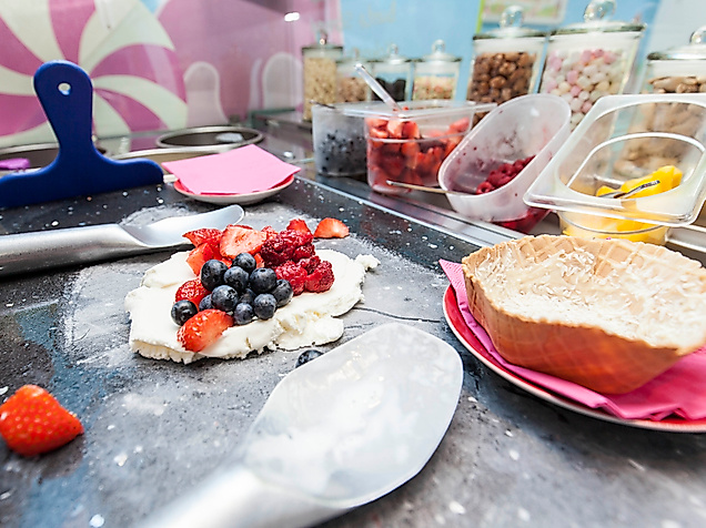 Eis wird im Eiscafé Schlecks mit frischen Beeren und Toppings auf einer kalten Platte zubereitet.