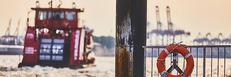 HADAG-Fähre im Hamburger Hafen, aufgenommen vom Anleger mit Rettungsring und Containerkränen im Hintergrund