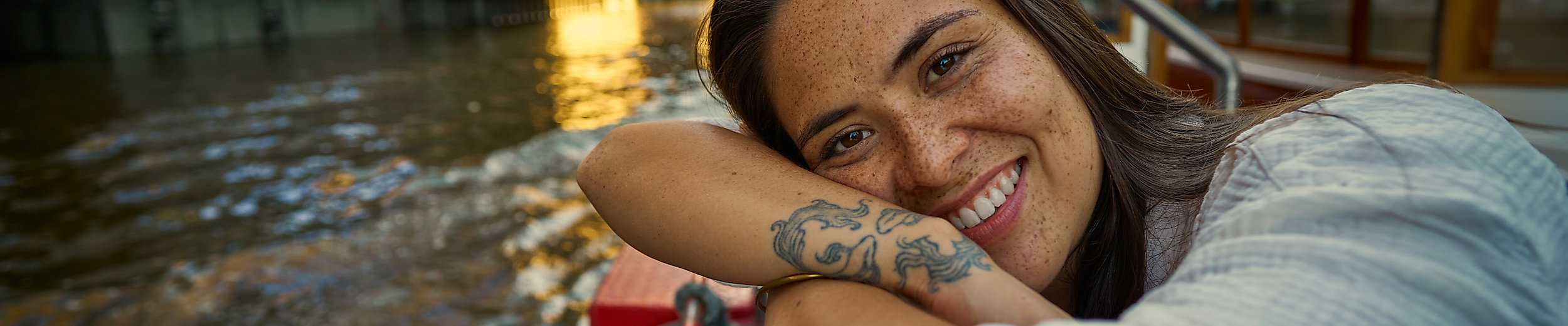 [Translate to English:] Eine junge Frau lehnt sich auf dem Deck eines Bootes an.