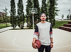 Junger Mann mit Basketball steht auf dem Sportfeld im Lohsepark vor einem Korb und hohen Bäumen