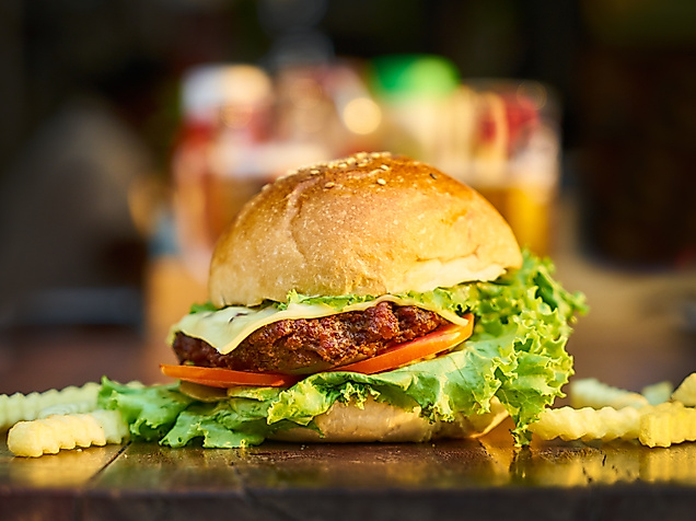 Saftiger Cheeseburger mit Salat und Tomate, serviert mit Pommes auf dunklem Tisch