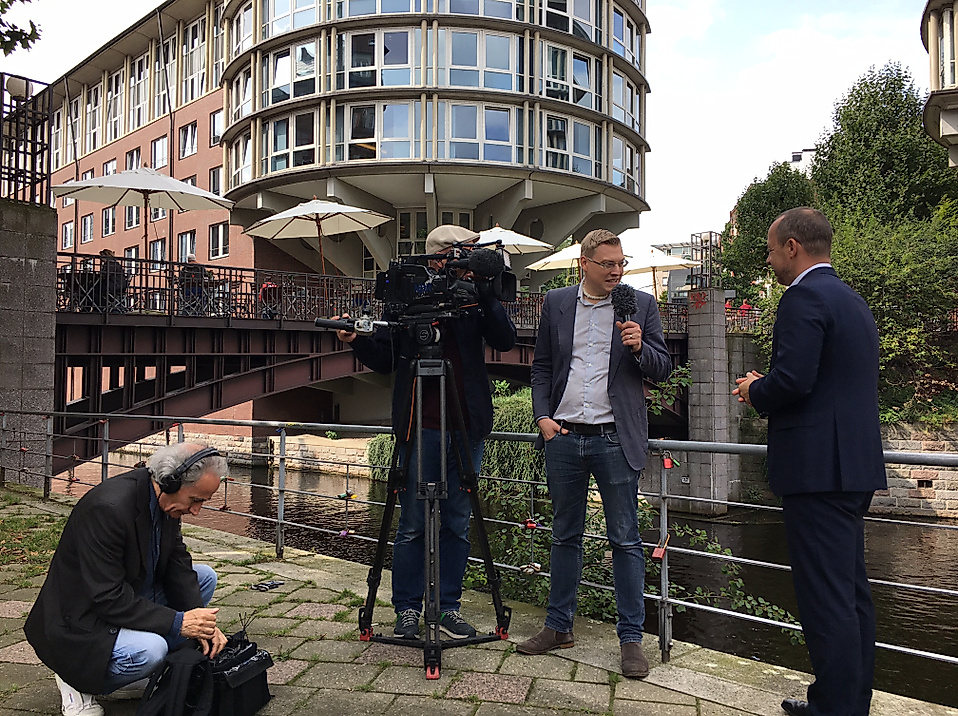 Interview mit Geschäftsführer Michael Otremba am Wasser, Kamerateam bei Dreharbeiten vor moderner Hamburger Architektur