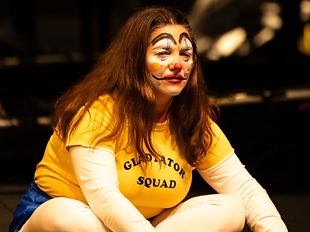 A person dressed as a clown is sitting on the stage.