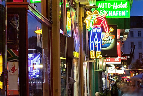 Leuchtende Neonreklamen und Schilder auf der Reeperbahn in Hamburg bei Abenddämmerung mit belebter Straße