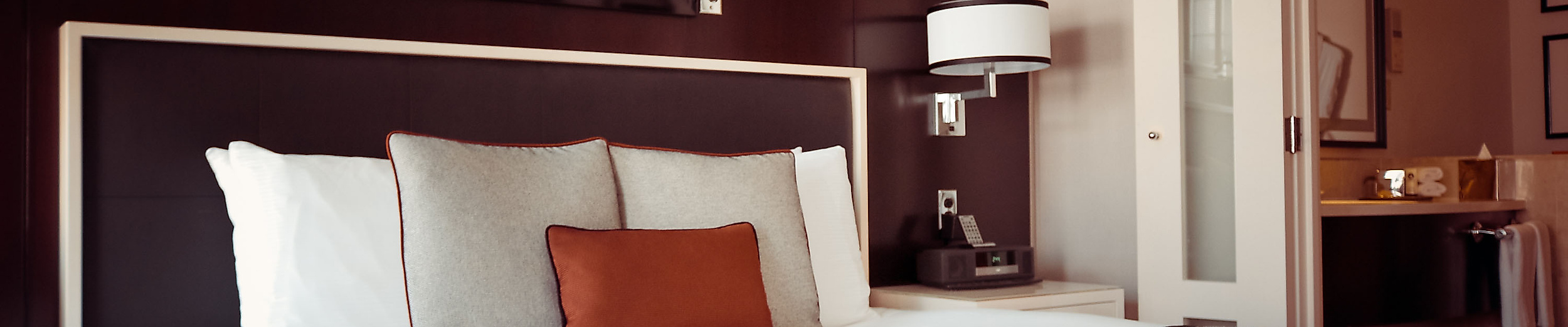 Modern eingerichtetes Hotelzimmer mit großem Bett, Zierkissen und offener Verbindung zum Badezimmer.