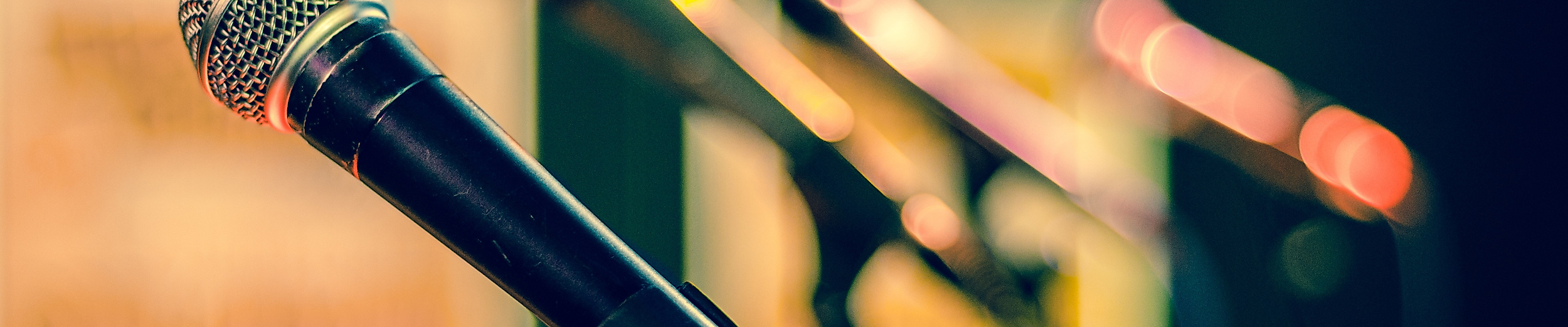 Nahaufnahme eines Mikrofons auf Bühne mit unscharfem Hintergrund in Konzertatmosphäre.