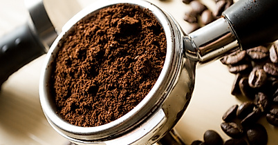 Frisch gemahlener Kaffee im Siebträger, umgeben von gerösteten Bohnen auf hellem Untergrund