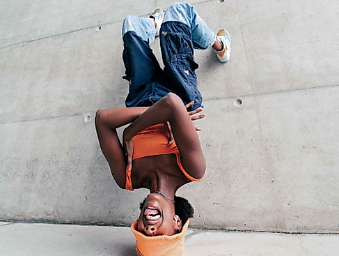 Eine junge Frau die kopfüber an einer Wand lehnt und Grimassen schneidet