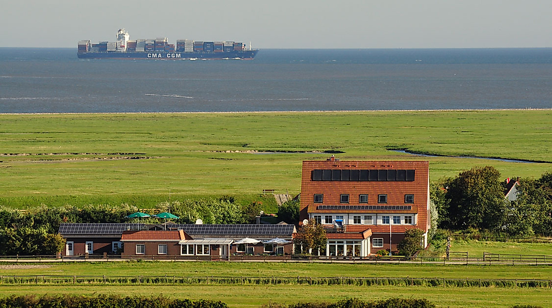 Gasthaus Nige Hus auf Neuwerk vor grüner Salzwiese mit Blick auf die Nordsee und vorbeifahrendes Containerschiffk