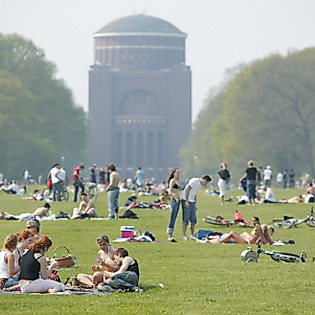 Zahlreiche Menschen entspannen auf der großen Wiese im Stadtpark mit Blick auf das Planetarium Hamburg