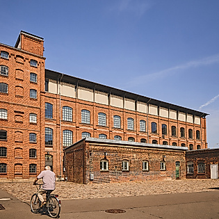 Backsteingebäude des Museums der Arbeit in Hamburg bei Sonnenschein mit Besucher:innen im Außenbereich