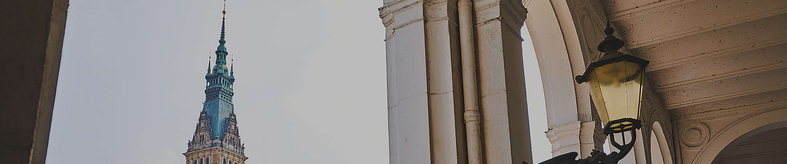 Blick durch die Alsterarkaden auf das Hamburger Rathaus mit grünem Kupferdach und Turm bei Tageslicht