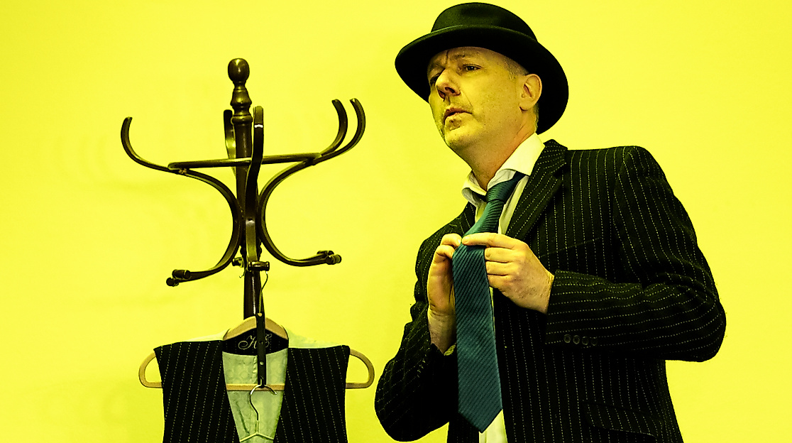 Mann mit Anzug und Hut vor gelbem Hintergrund