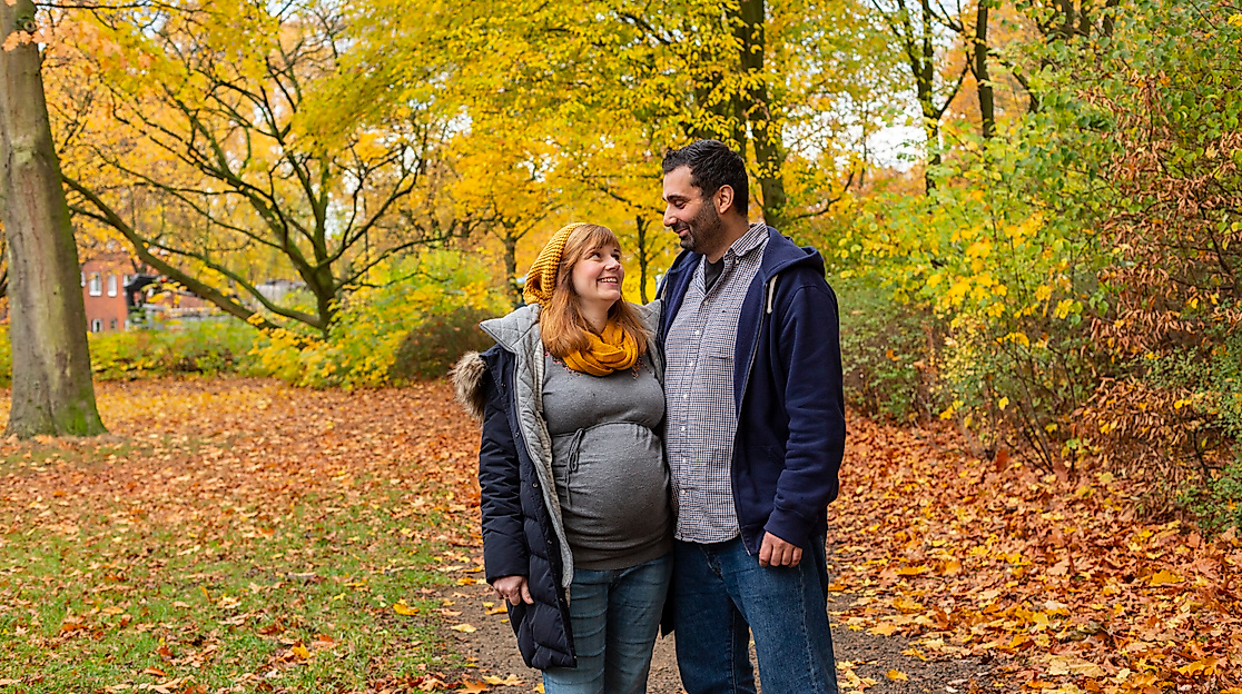 Paar im herbstlich bunten Park, eng umschlungen und lächelnd beim Spaziergang durch Laub in Hamburg