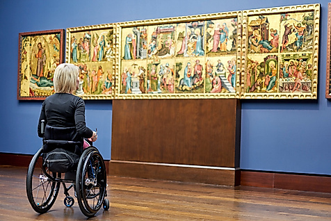 Rollstuhlfahrerin betrachtet ein mehrteiliges historisches Gemälde in der barrierefreien Hamburger Kunsthalle.