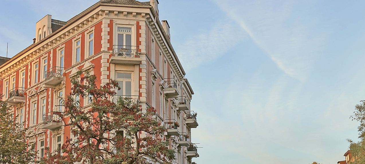 Gründerzeitfassade in Hamburg-Eppendorf im Abendlicht vor herbstlich gefärbten Bäumen und blauem Himmel