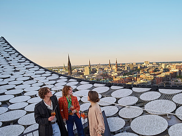Auf dem Dach der Elbphilharmonie Hamburg stehen drei Leute. Schauen über die Stadt