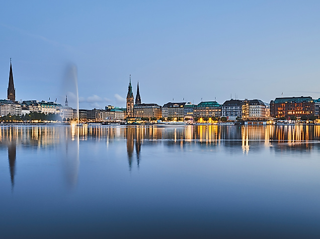 Binnenalster bei Nacht mit beleuchteter Stadtsilhouette, Alsterfontäne und Spiegelung im Wasser