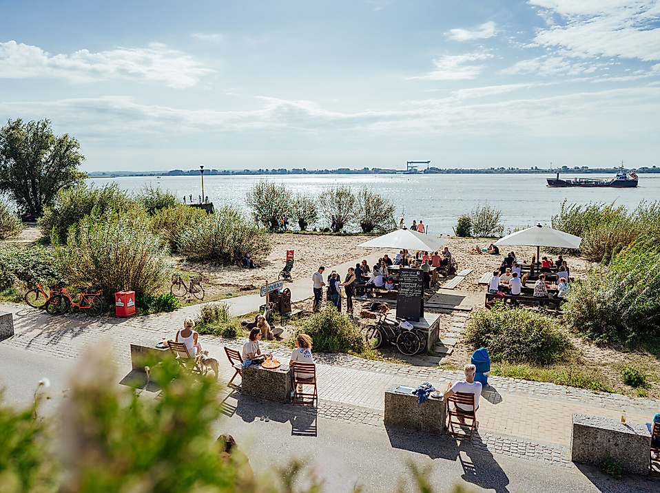 Ausflugslokal am Elbstrand mit Blick auf die Elbe und vorbeifahrende Schiffe bei Sommerwetter