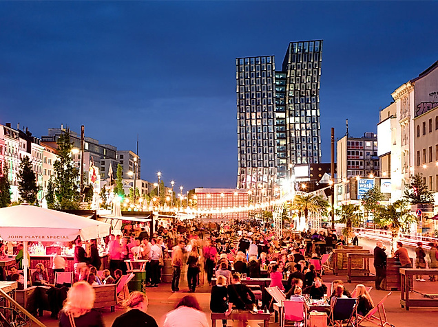 Belebte Abendstimmung auf der Reeperbahn in Hamburg mit Lichterketten, Straßencafés und tanzenden Türmen im Hintergrund
