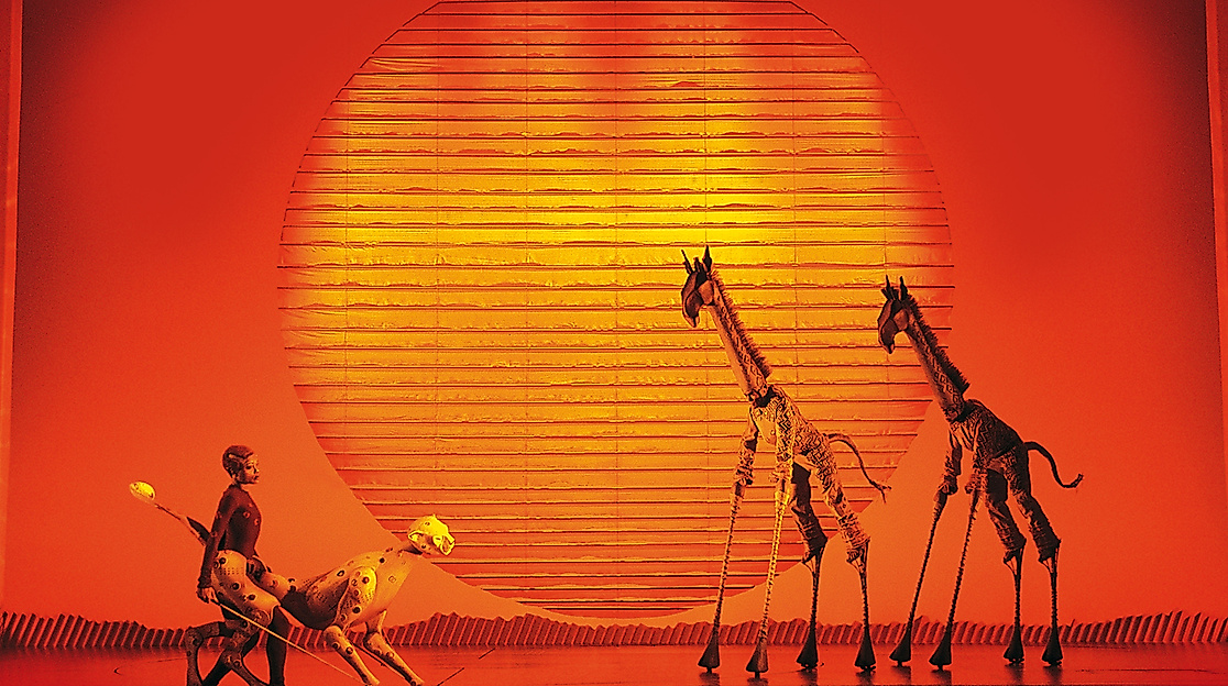 Szenenbild König der Löwen: 2 Giraffen und ein Löwe bei Sonnenuntergang