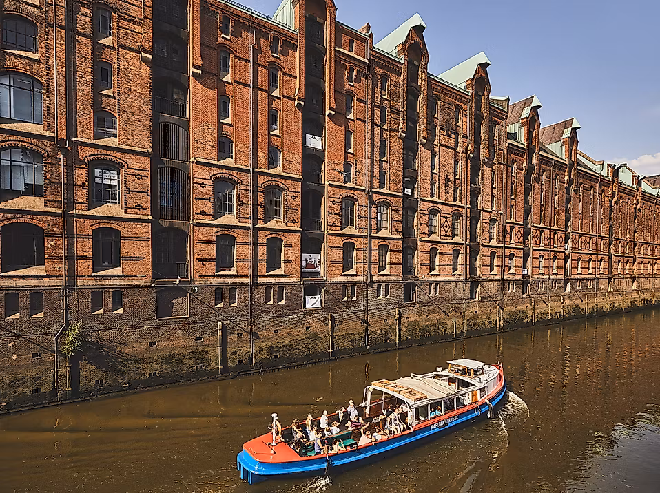 Barkasse fährt durch einen Fleet der Speicherstadt entlang roter Backsteinfassaden bei Sonnenschein