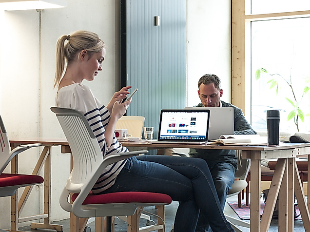 Zwei Personen arbeiten entspannt in einem modernen, hellen Büro mit Laptops und Smartphones