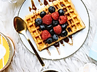 Waffel mit frischen Beeren und Schokosoße auf Teller, serviert mit Eiscreme und goldfarbenem Löffel