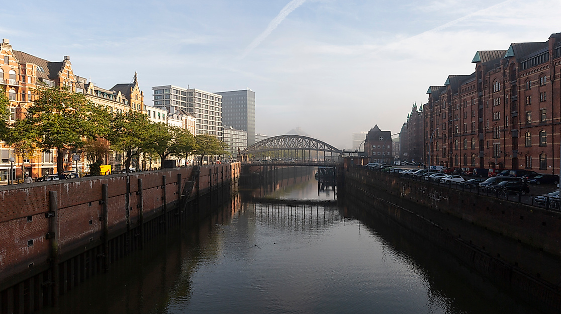 Kanal in der Hamburger Speicherstadt mit Backsteinfassaden, Brücke und Blick auf die Hafencity