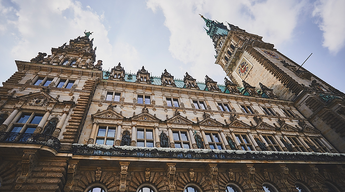 Hamburger Rathaus aus Untersicht mit reich verzierter Fassade und Rathausturm vor blauem Himmel