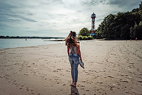 Frau trägt Kind am Elbstrand Wittenbergen, barfuß im Sand mit Leuchtturm im Hintergrund