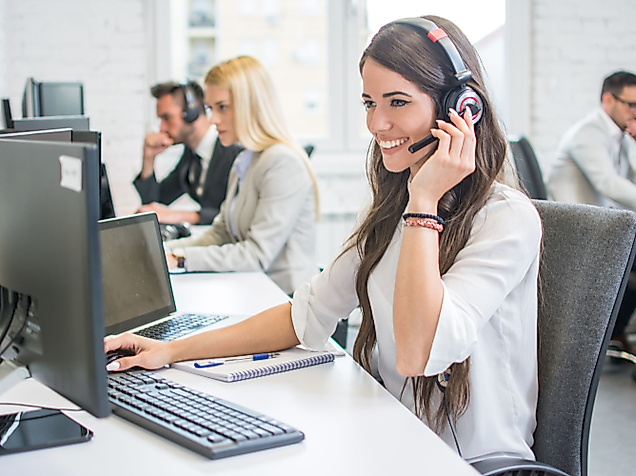 Mitarbeiterin im Hamburg Service Center telefoniert mit Headset am Arbeitsplatz, weitere Personen im Hintergrund