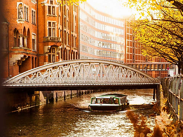 Sonnenlicht über Brücke in Hamburgs Speicherstadt mit Boot auf herbstlich gefärbtem Fleet.
