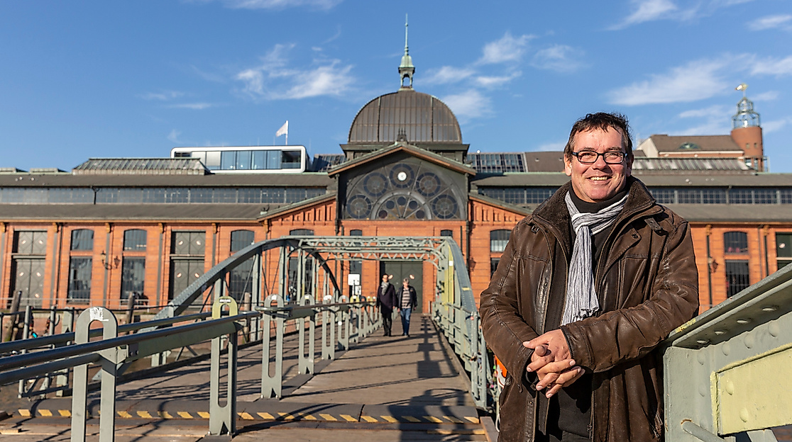 Person auf Brücke vor der Hamburger Fischauktionshalle bei Sonnenschein und blauem Himmel