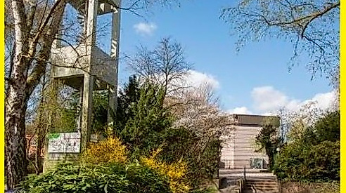 Kirchturm mit grünen Sträucher und im Hindergrund Kirchengebäude