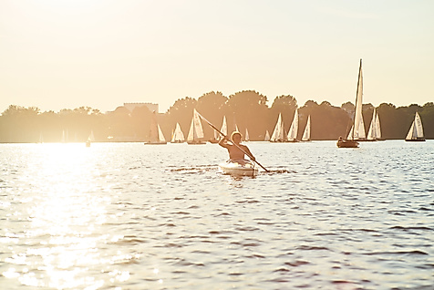 Person paddelt im Kanu auf der Alster bei Sonnenuntergang, umgeben von zahlreichen Segelbooten