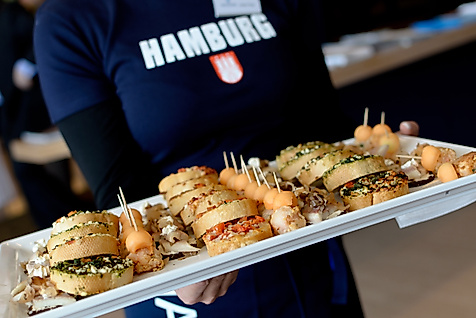 Person mit Hamburg-Shirt serviert Platte mit Fischbrötchen und Fingerfood-Häppchen