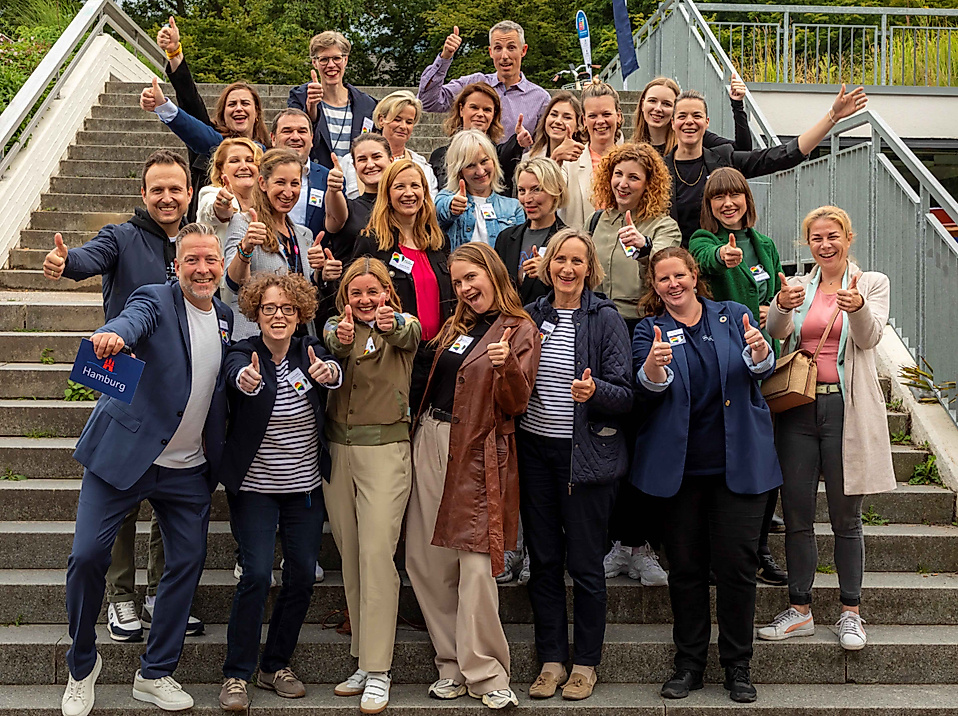 Gruppenfoto fröhlicher Mitarbeiter:innen beim HHT-Partnertreffen 2024 auf einer Außentreppe