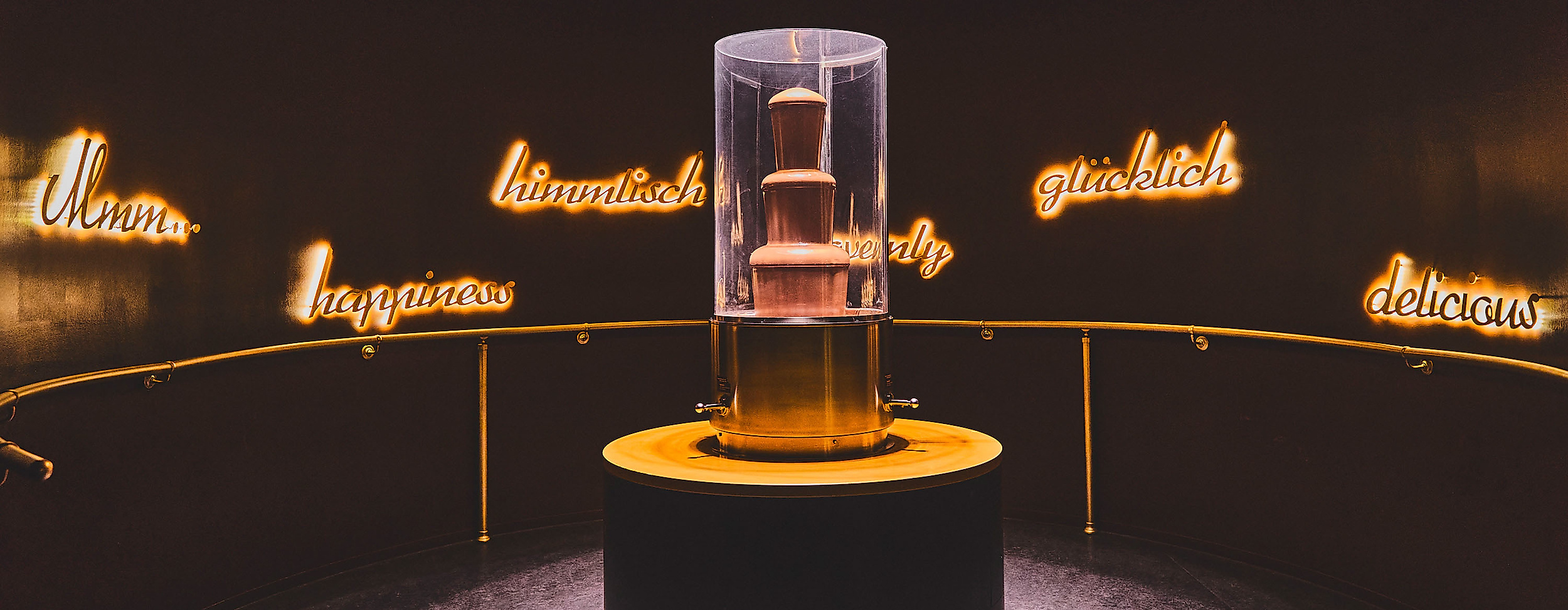 Beleuchteter Schokobrunnen im dunklen Ausstellungsraum des Chocoversums Hamburg, zentral in Szene gesetzt