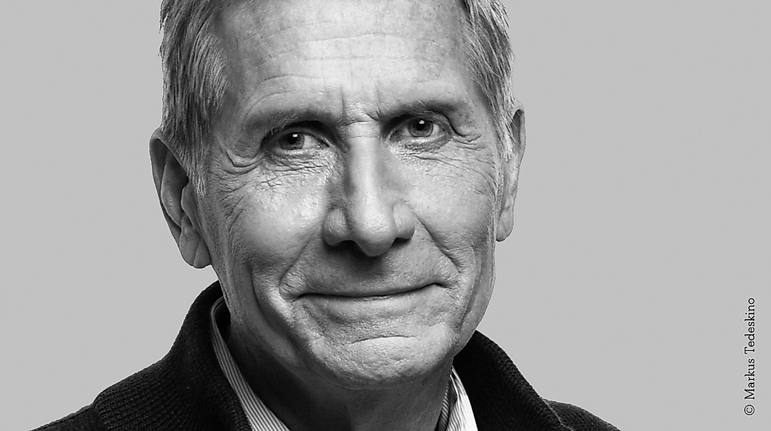 Black-and-white portrait photo of an older male-identified person with short hair and a dark collar.