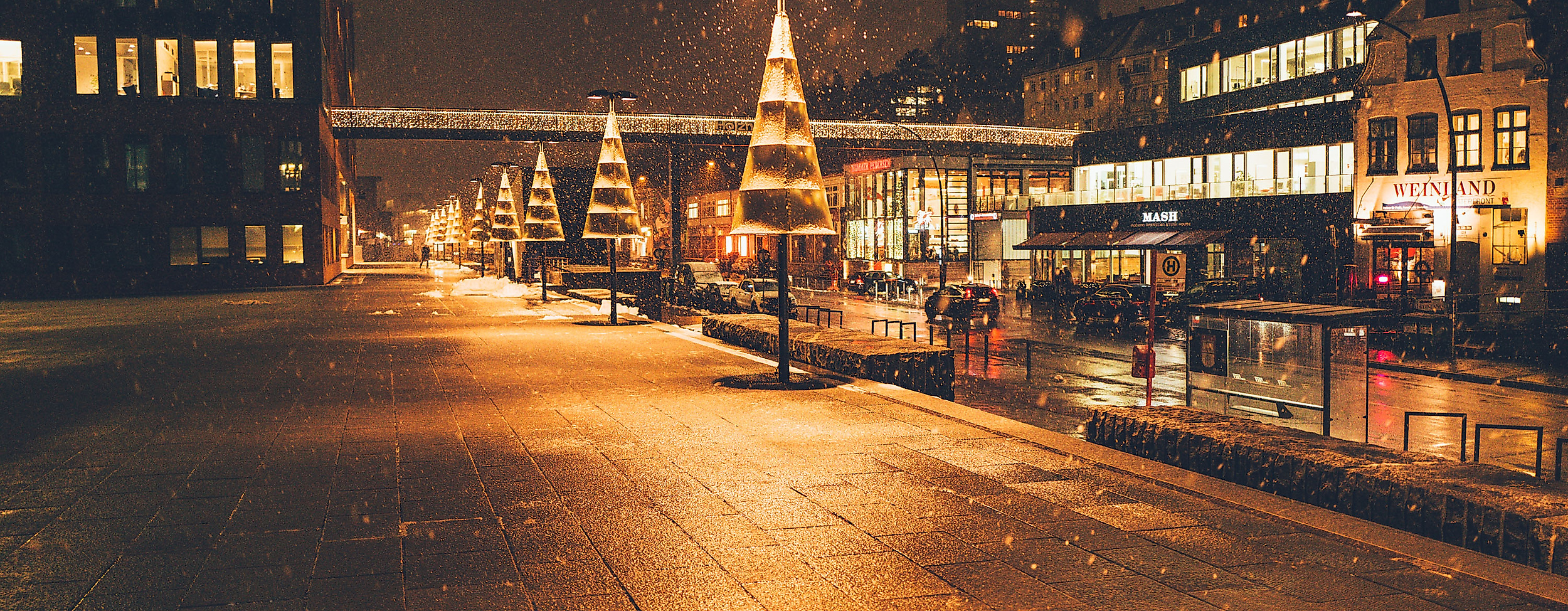 Christmas lights reflecting on wet cobblestones at night in a festively lit Hamburg street