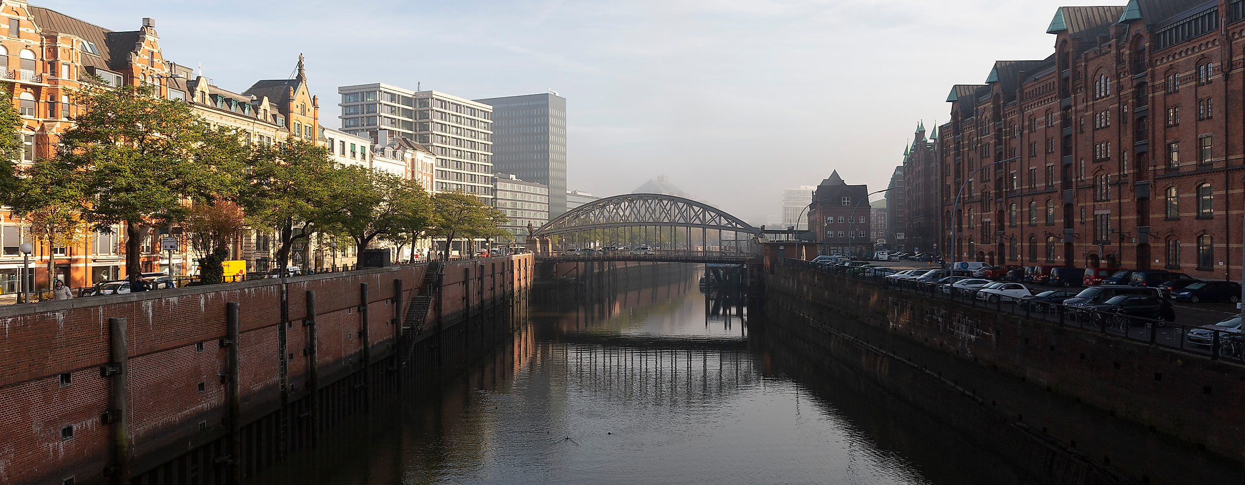 Kanal in der Hamburger Speicherstadt mit Backsteinfassaden, Brücke und Blick auf die Hafencity