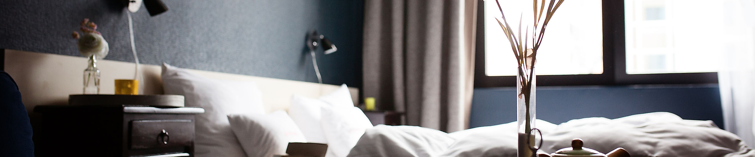 Gemütlich eingerichtetes Schlafzimmer mit Doppelbett, dunklen Wänden und Tageslicht durch ein großes Fenster.