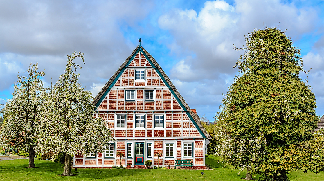 Traditionelles Fachwerkhaus im Alten Land mit blühenden Obstbäumen vor blauem Himmel.