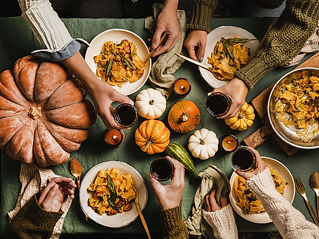 mit Rotwein anstoßende Hände über einem herbstlich gedeckten Tisch