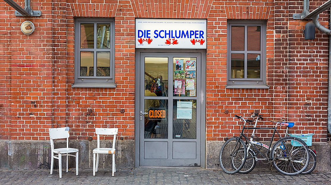 Backsteinfassade mit Glastür, zwei weißen Stühlen und abgestellten Fahrrädern auf gepflastertem Boden