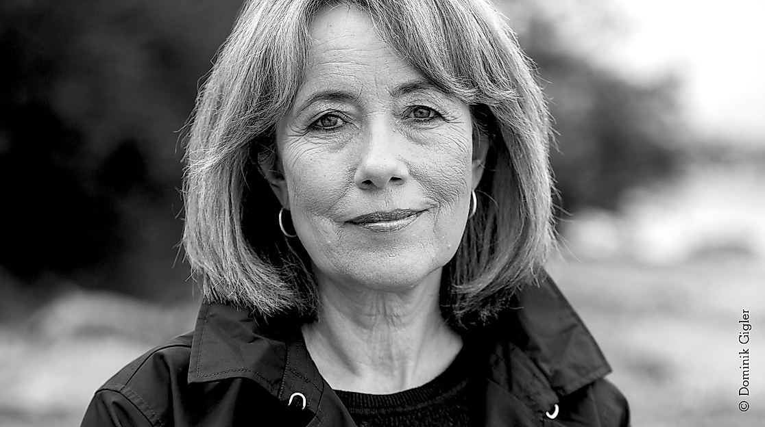 Black-and-white portrait photo of a middle-aged woman with a bob hairstyle. She is wearing hoop earrings and a dark jacket.