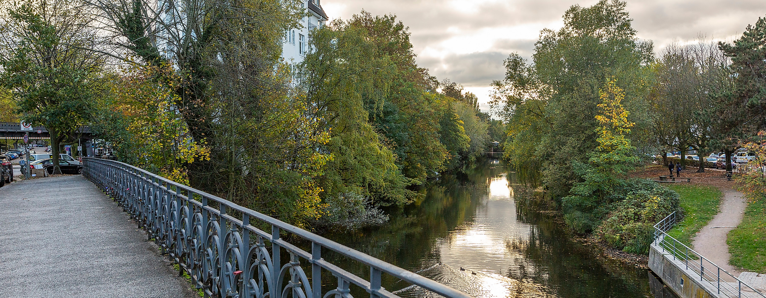 Fußgängerbrücke über dem Isebekkanal in Hamburg-Eimsbüttel mit Bäumen und Spazierweg bei Abendlich